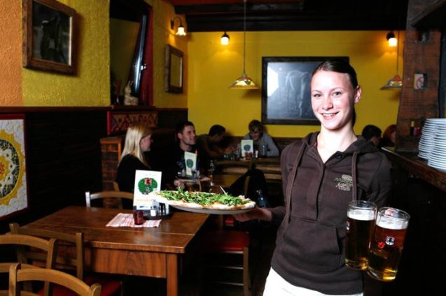 A waitress posing with a pizza and a pair of beers inside Pizzeria Rustika in Bled