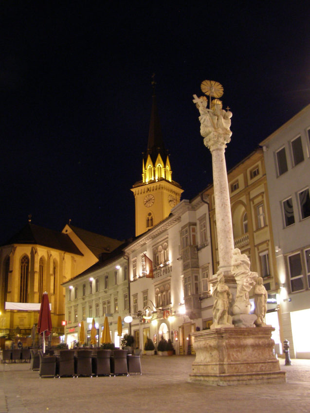 Villach main square Hauptplatz at night with the Holy Trinity column and the church of St. Jacob