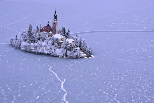 A group of people walking across the frozen Lake Bled to the picturesque island with a church in the middle