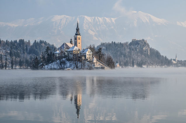 Lake Bled with its island with a church and a medieval castle on top of a rocky cliff in winter