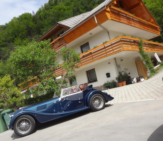 A couple of British guests with a Morgan Roadster in front of Fine Stay Apartments in Slovenia