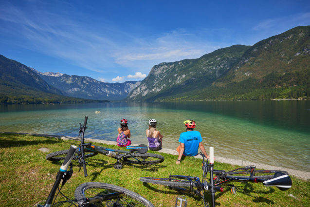 A group of cyclists resting an enjoying views of Lake Bohinj in summer