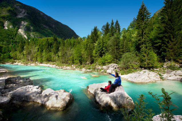 A couple sitting on a big rock in the middle of Soca River in Slovenia