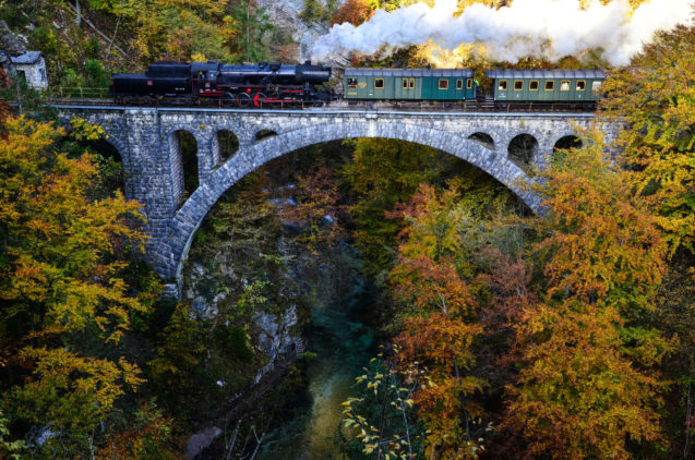 A steam-powered museum train crossing the bridge over the Radovna river in the Vintgar Gorge in autumn